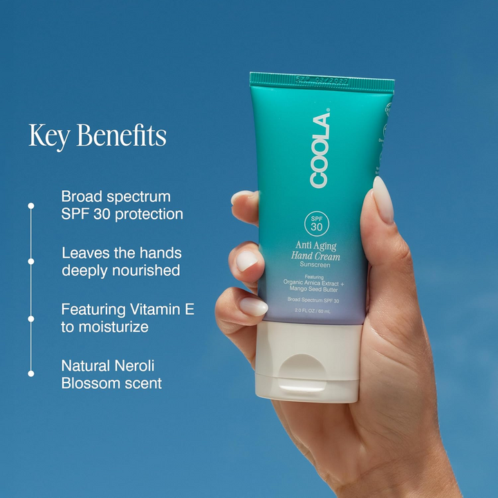 Hand holding a tube of Coola hand cream with key benefits listed on a blue background