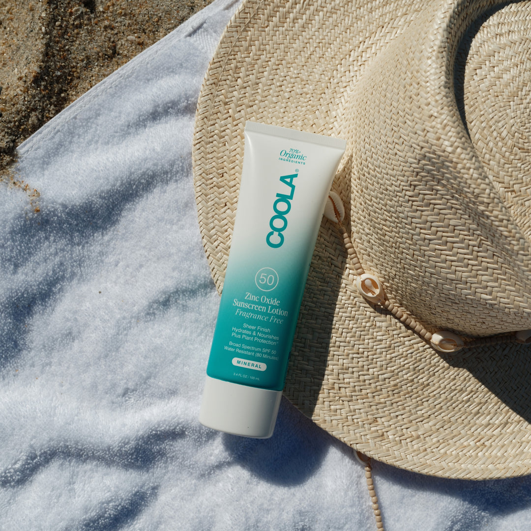 COOLA  Mineral Body Organic Sunscreen Lotion SPF 50 - Fragrance Free with a beach towel and beach hat