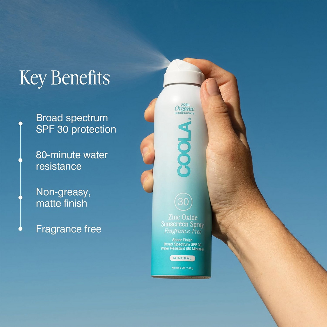 COOLA Mineral Body Organic Sunscreen Spray SPF 30 Fragrance Free being held with key benefits listed on a blue background
