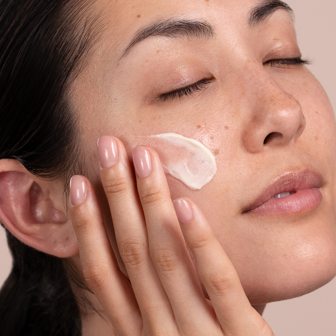 Woman applying Eminence Organics Apricot Calendula Nourishing Cream  to her face with a neutral background