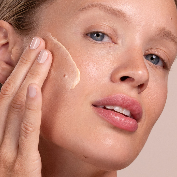 Close-up of a woman applying Eminence Organics Apricot Whip Moisturizer to her face with a neutral background