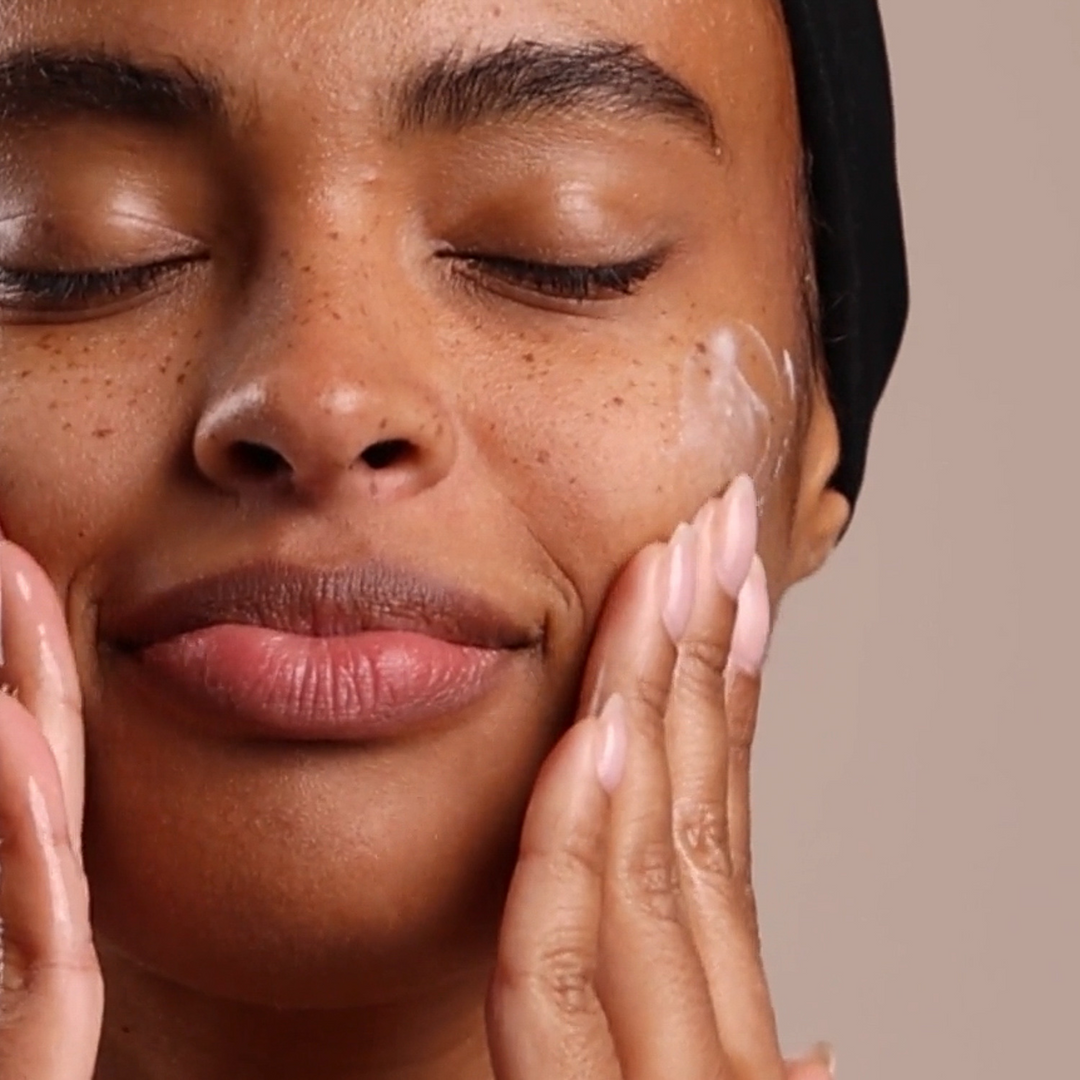 Woman applying eminence orgniacs calm skin chamomile moisturizer to her face with a neutral background