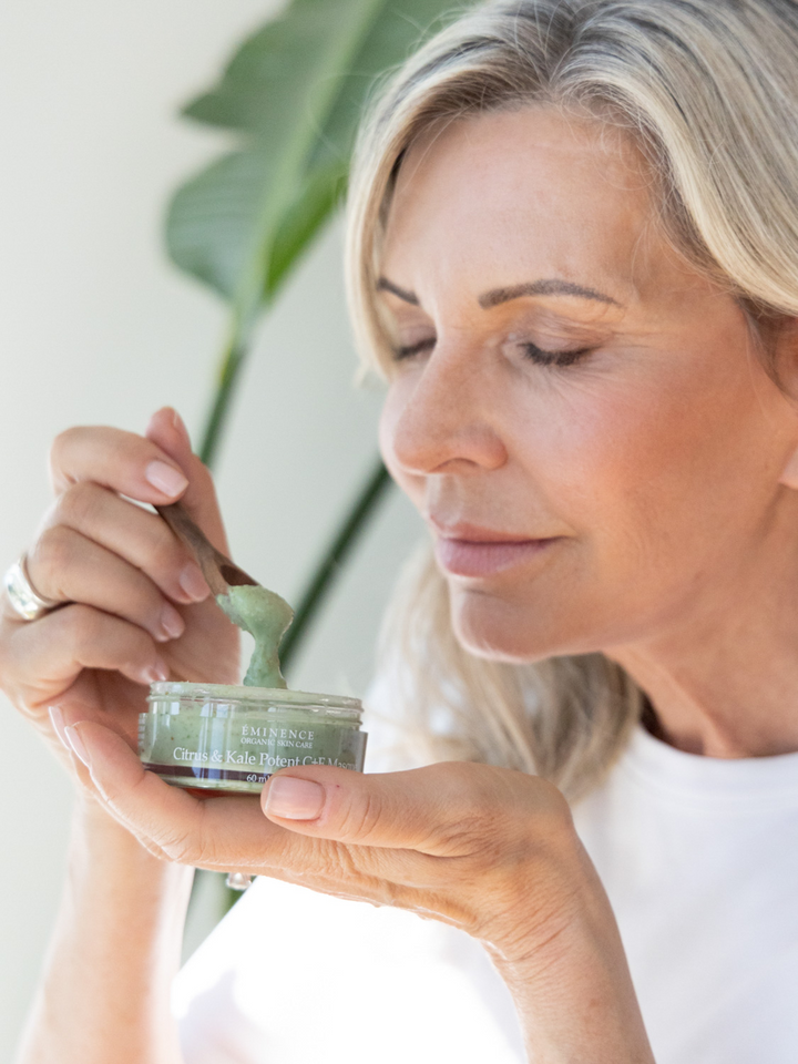 Woman holding a jar of Eminence Organics Citrus &amp; Kale Potent C+E Masque with a plant in the background
