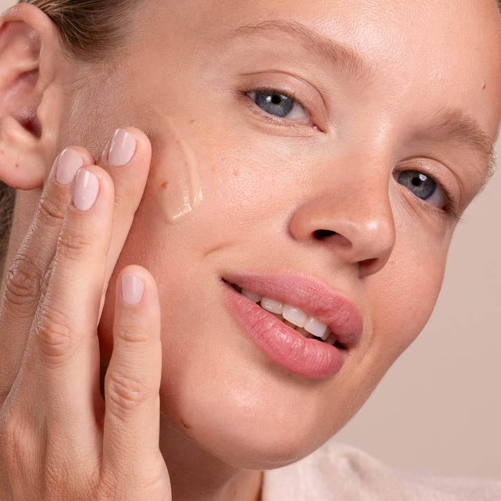 Close-up of a woman applying Eminence Organics Cornflower Recovery Serum to her face.