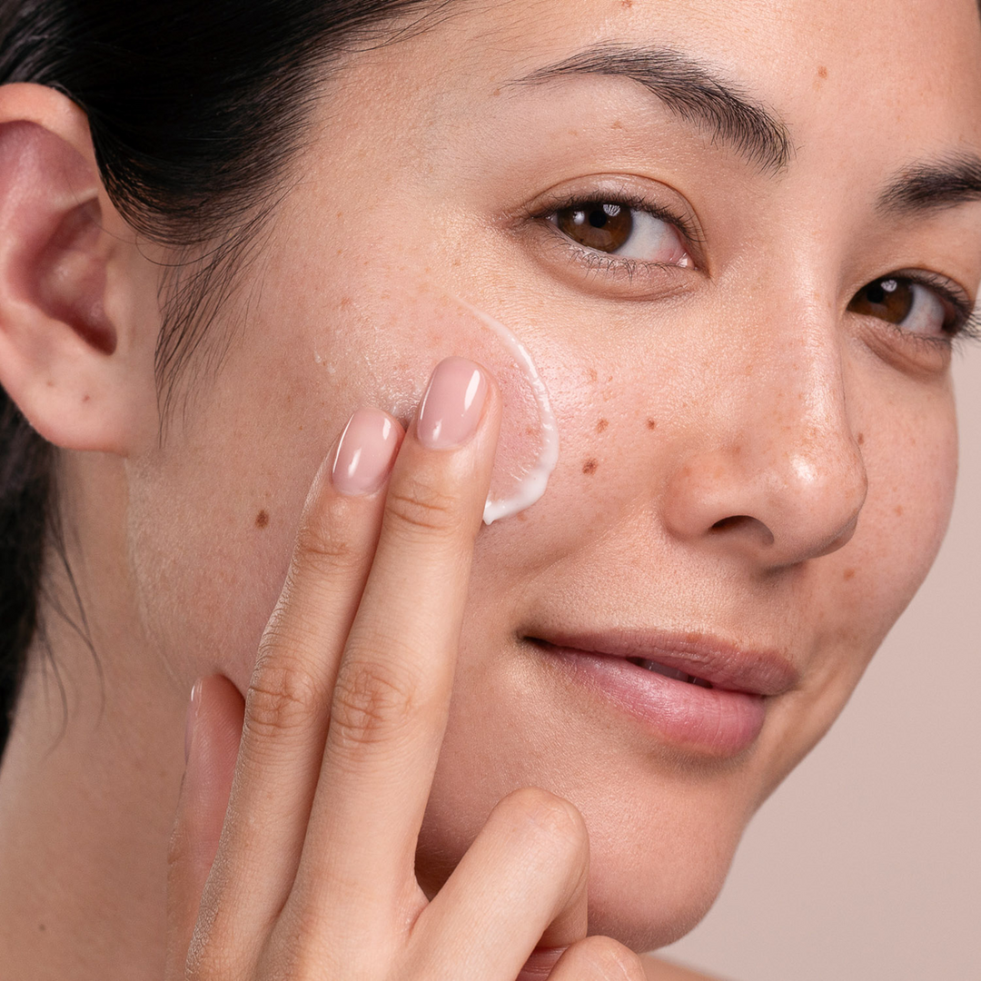 Woman applying Eminence Organics Echinacea Recovery Cream to her face with a neutral background