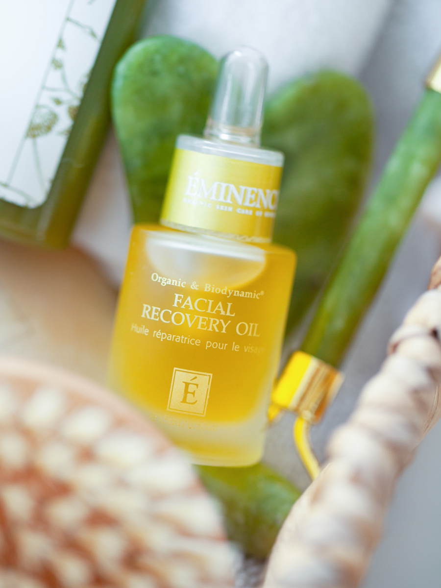 Facial recovery oil bottle with green leaves and seashells in the background