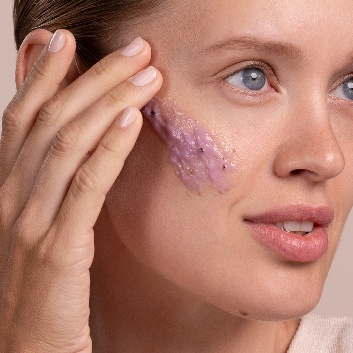 Woman applying Eminence Organics Firm Skin Acai Masque to her face with a neutral background