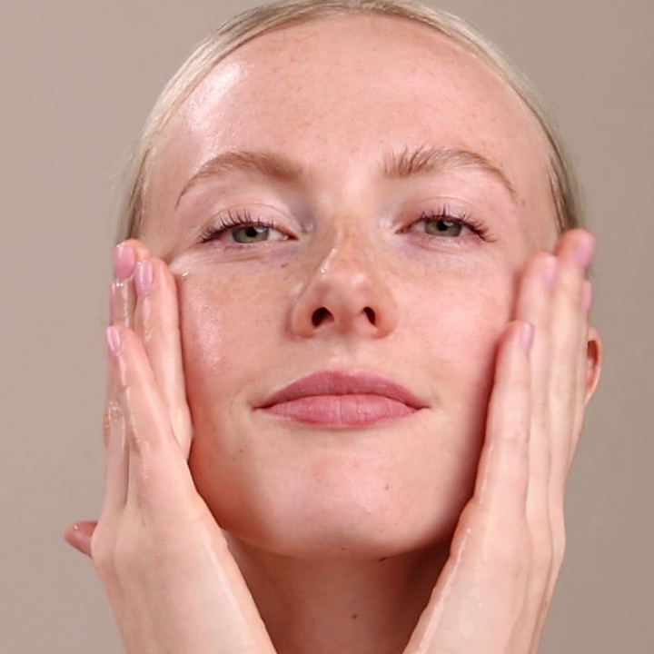 Woman using Eminence Organics Firm Skin Starter Set against a neutral background