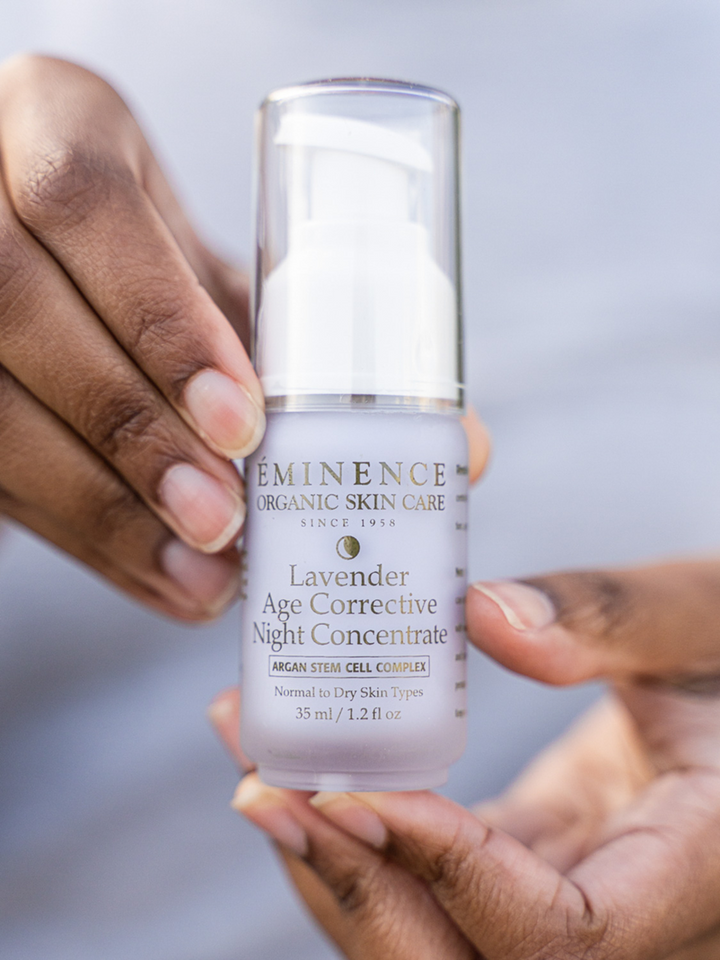 Hand holding a bottle of Eminence Organic Skin Care Lavender Age Corrective Night Concentrate against a neutral background.