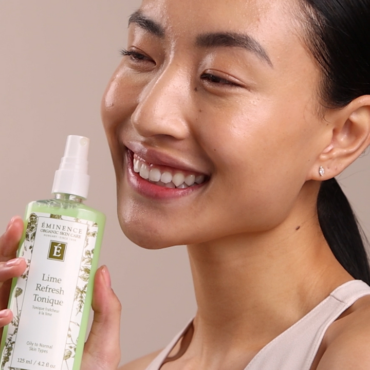 Woman holding a bottle of Eminence Lime Refresh Tonic with a neutral background