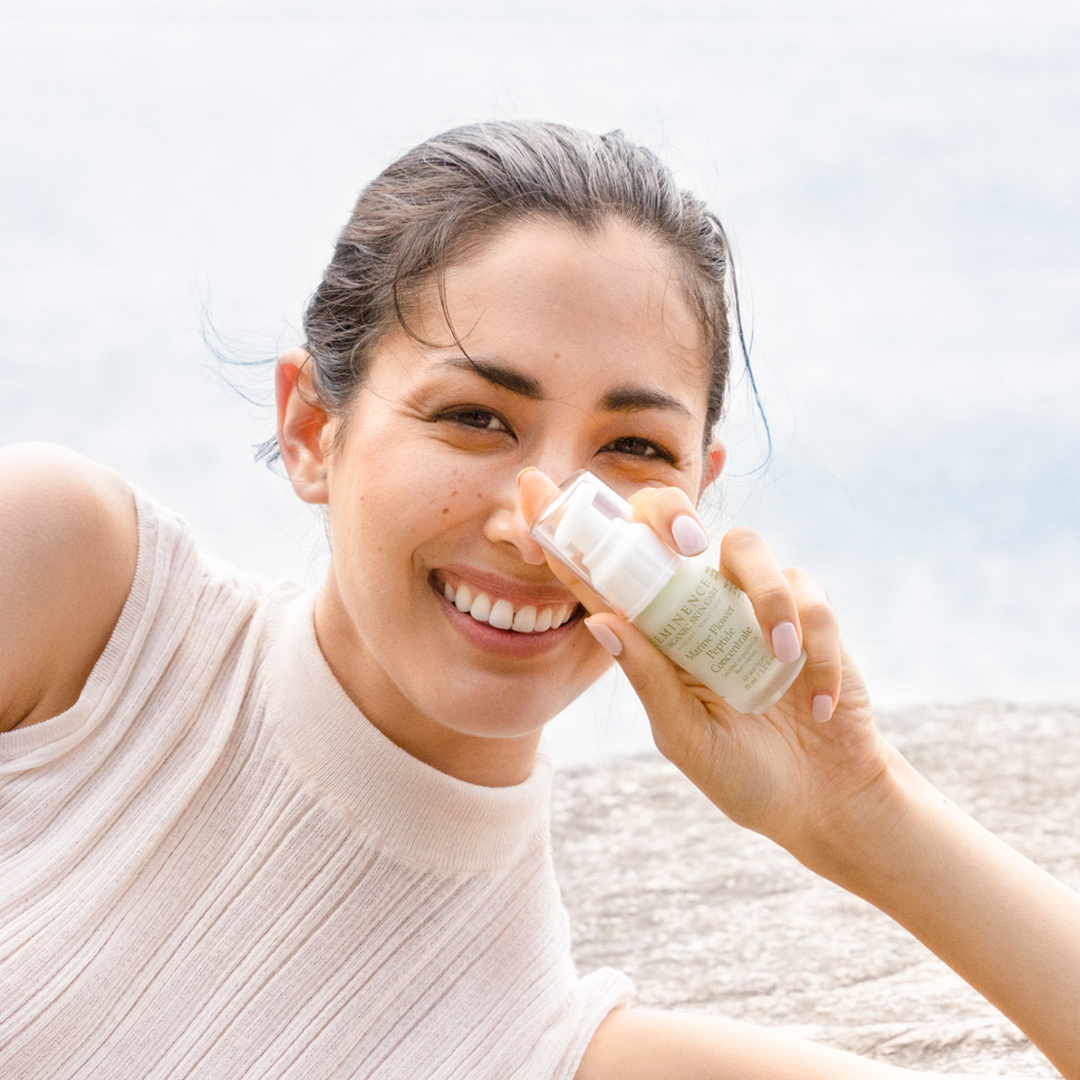 woman holding Eminence Organics Marine Flower Peptide Concentrate on a beach