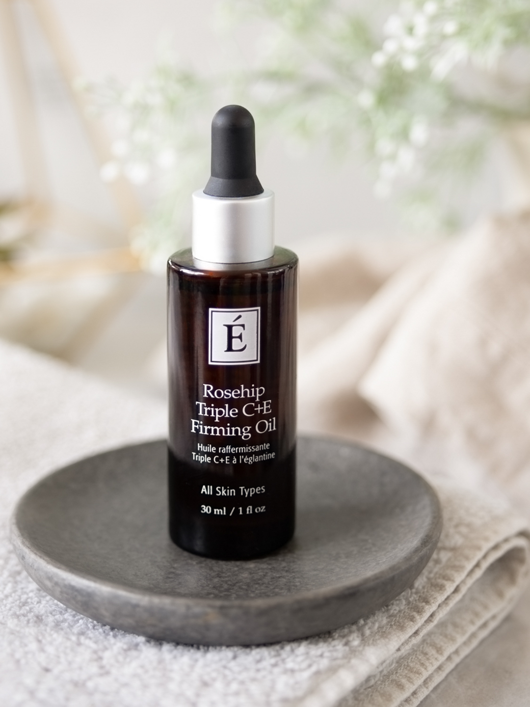Rosehip Triple C+E Firming Oil bottle on a gray plate with a blurred natural background