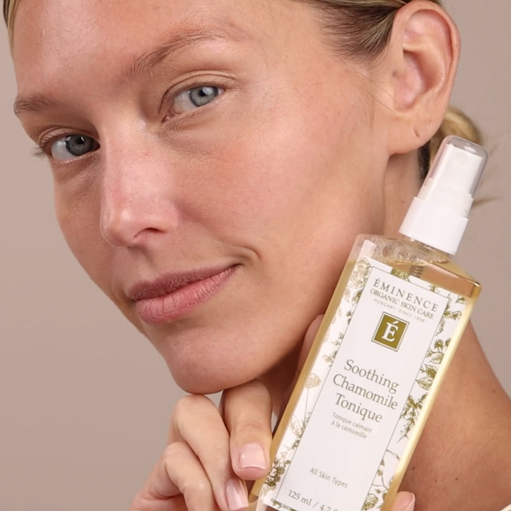 Woman holding a bottle of Eminence Soothing Chamomile Tonique against a neutral background