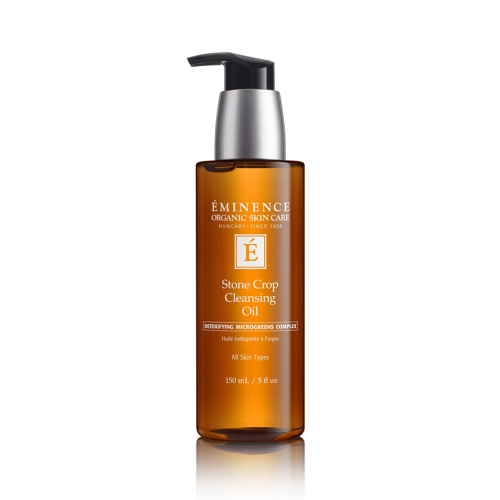 A bottle of Éminence Organic Skin Care Stone Crop Cleansing Oil on a white background with a soft reflection. The bottle is amber brown with a black and silver pump dispenser.