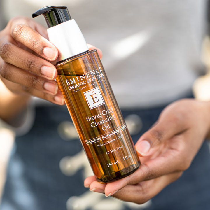Person holding a bottle of Eminence Organic Skincare Stone Crop Cleansing Oil.