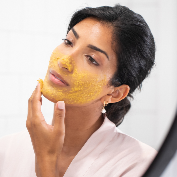 woman applying Eminence Organics Turmeric Energizing Treatment on her face