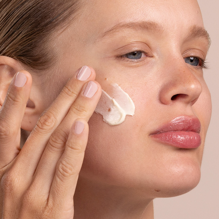 Woman applying Eminence Organics Yellow Sweet Clover Anti-Redness Masque to her face with a neutral background