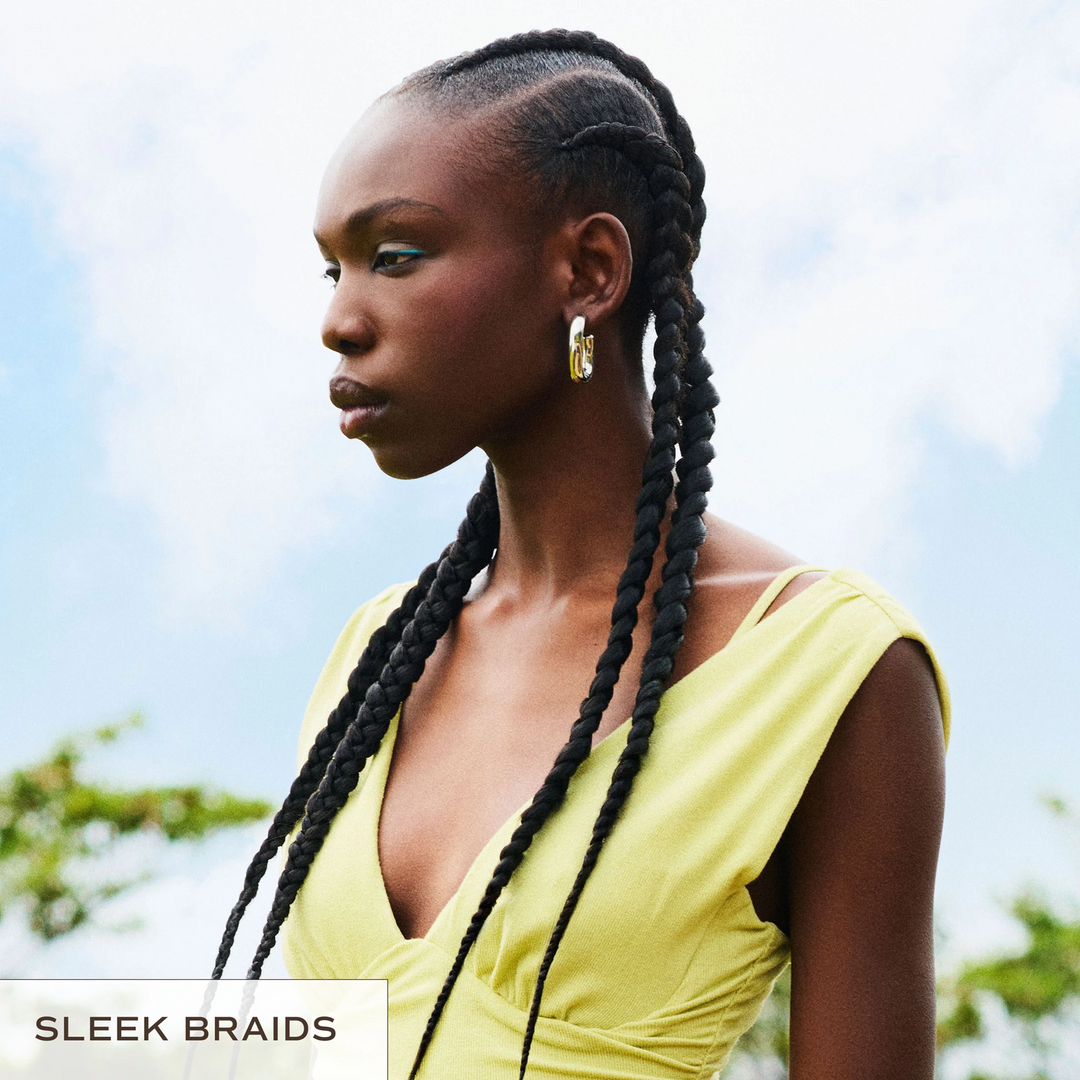 Woman with sleek braids wearing a yellow top against a blurred natural background for INNERSENSE Organic Beauty Inner Reflection Sculpting Pomade sleek braids