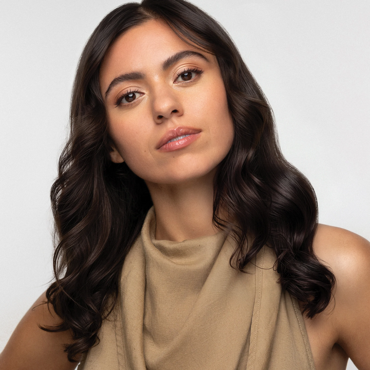 Model with long, dark brown hair styled in glossy, loose waves against a light gray background