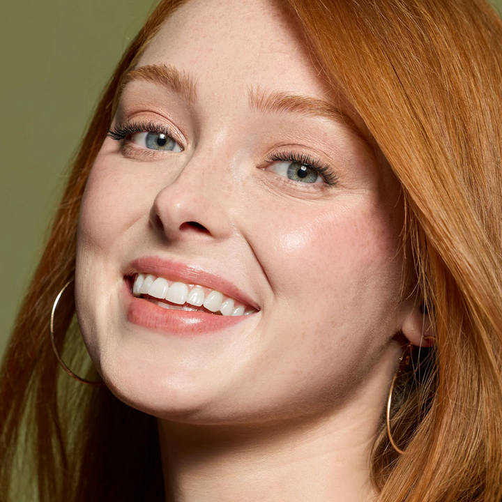Smiling red-haired model with a glossy pink lip finish showcasing Jane Iredale Just Kissed pH Lip Oil