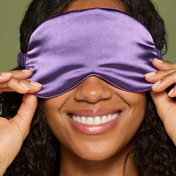 Smiling model wearing the purple sleep mask from the Jane Iredale Well Rested Nighttime Recovery Kit