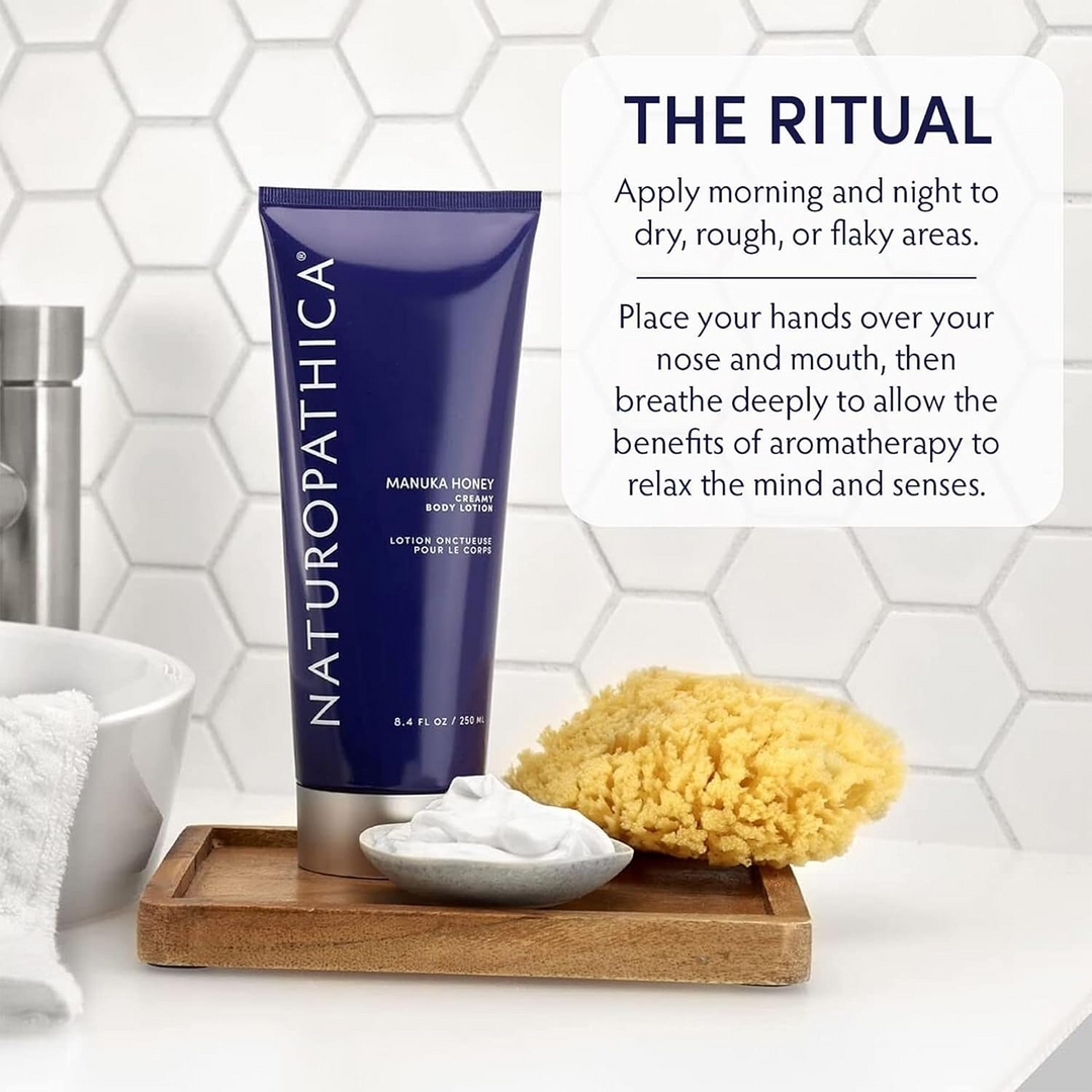 Naturopathica Manuka Honey Creamy Body Lotion on a wooden tray with a sponge and bowl against a tiled wall background.