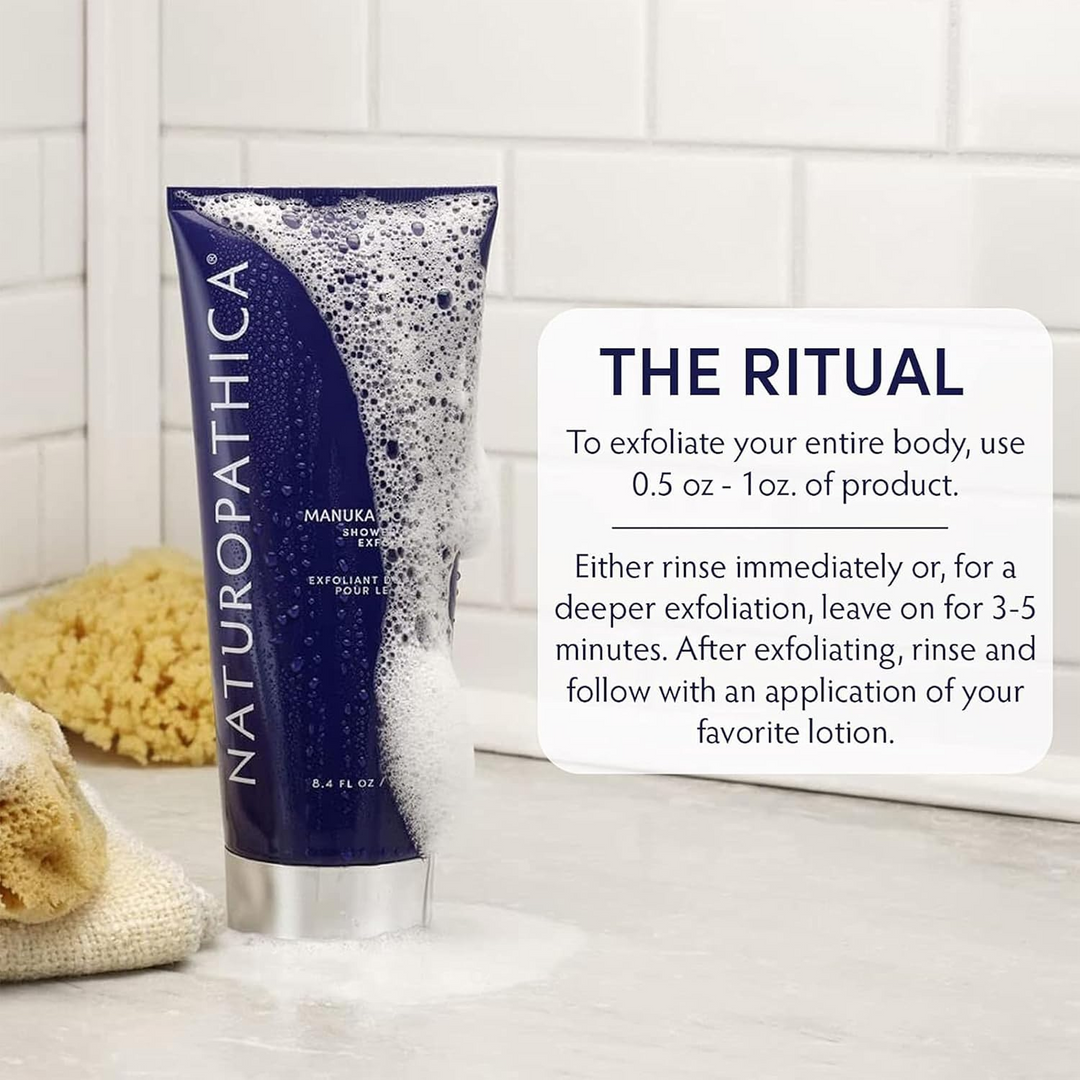 Naturopathica Manuka Honey Shower Body Exfoliator tube standing on a bathroom counter with foam, a sponge, and a white tiled wall in the background. A text box reads &