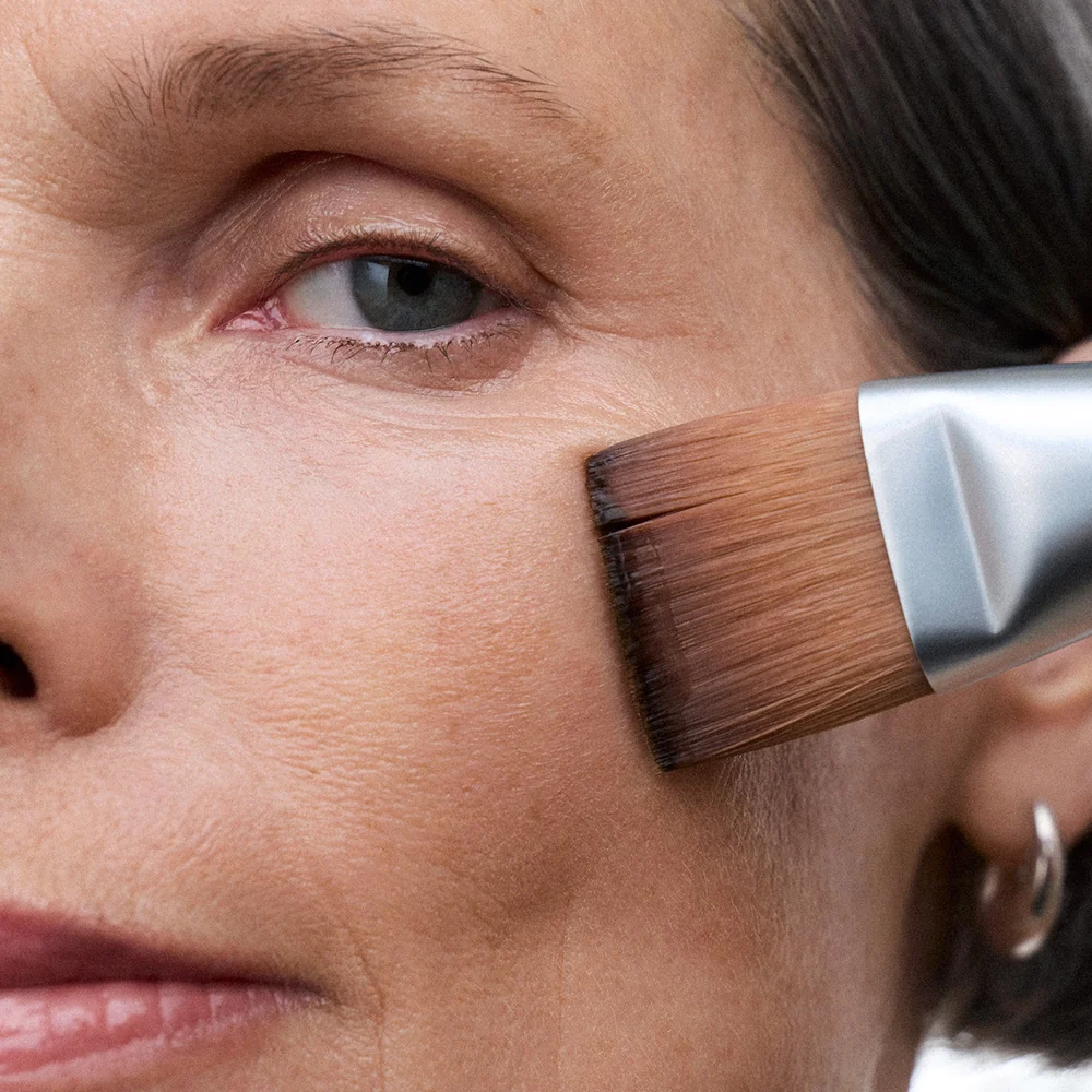 Close-up of a woman applying makeup with NuFACE Clean Sweep Applicator Brush to her face.