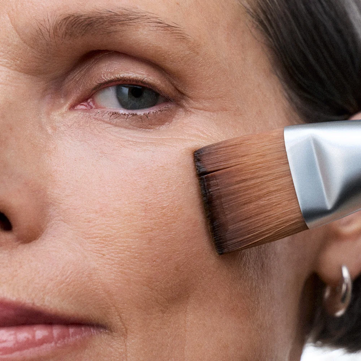 Close-up of a woman applying makeup with NuFACE Clean Sweep Applicator Brush to her face.