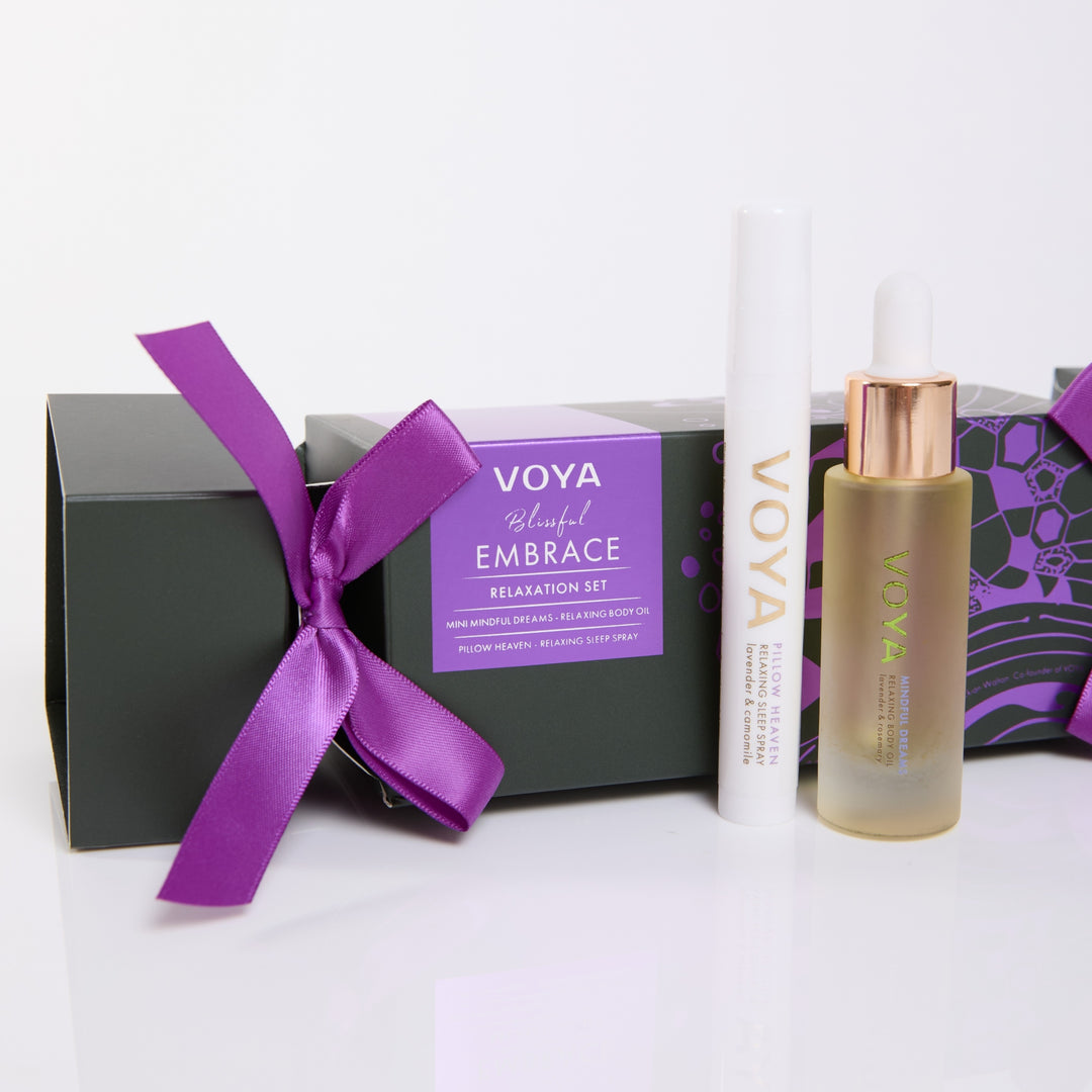 Close-up of VOYA Mindful Dreams body oil and Pillow Heaven sleep spray beside the purple-ribboned Blissful Embrace gift box.
