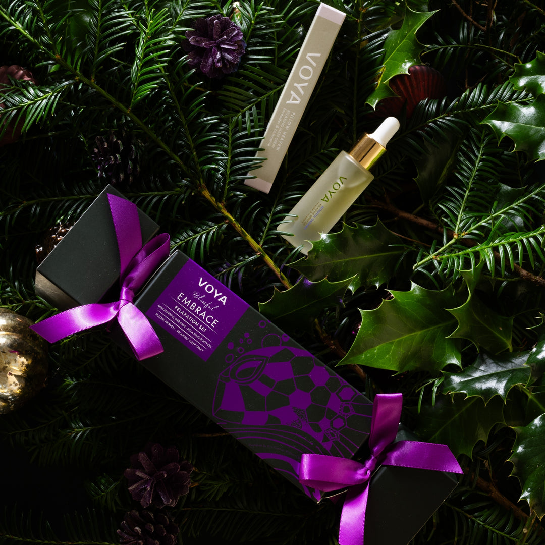 VOYA Blissful Embrace gift set nestled among evergreen branches, holly leaves and festive ornaments.
