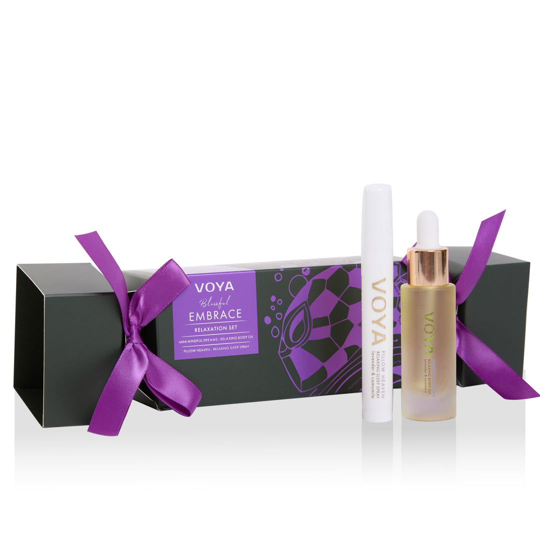 VOYA Blissful Embrace Relaxation Set with body oil, sleep spray and a cracker-shaped gift box tied with purple ribbons.
