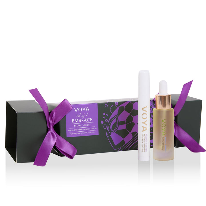 VOYA Blissful Embrace Relaxation Set with body oil, sleep spray and a cracker-shaped gift box tied with purple ribbons.
