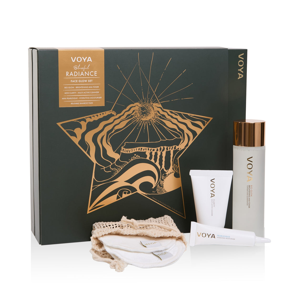 VOYA Blissful Radiance Face Glow Set with toner, cleanser, moisturiser and reusable pads beside a gold-star illustrated gift box.
