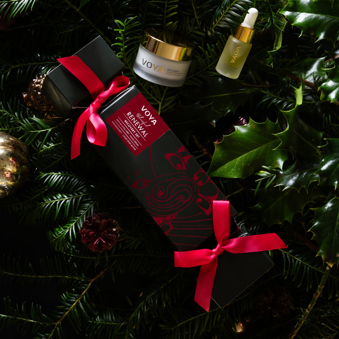 VOYA Blissful Renewal gift set nestled among evergreen branches, holly leaves and festive ornaments.
