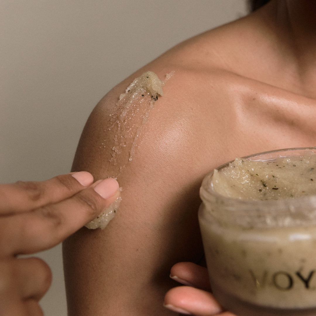 Person applying VOYA Iridescence Awakening Sugar Scrub to their shoulder while holding the open jar