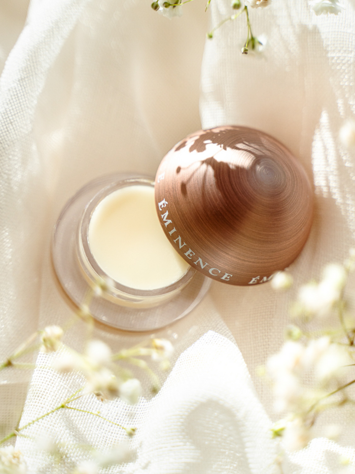 Cosmetic container with Eminence Organics Citrus Lip Balm on a soft fabric background