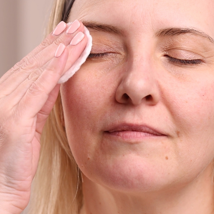 Woman cleaning her face with a cotton pad, close-up of her face.